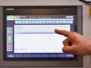 Mano che punta a un monitor touchscreen con interfaccia Siemens